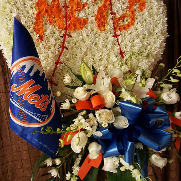Large white floral wreath with orange lettering and a Mets pennant