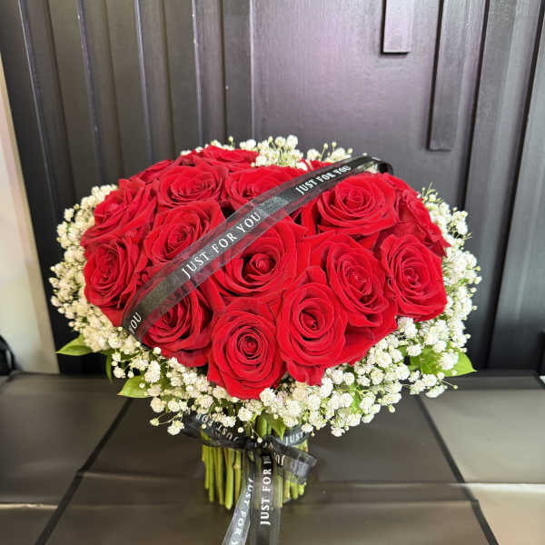 Hand-tied bouquet of red roses encircled by small white blooms with black Just For You ribbons.