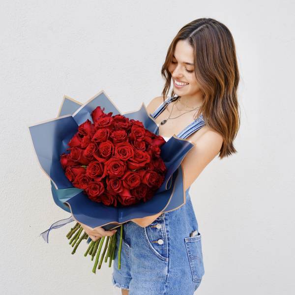 Woman holding a bouquet of red roses wrapped in blue paper