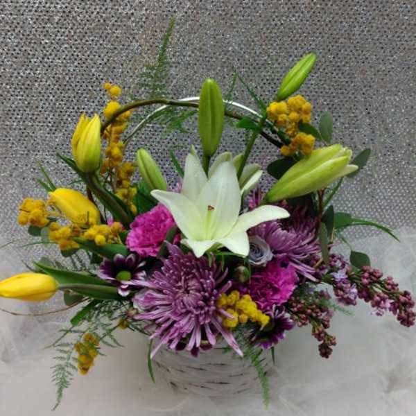 Basket arrangement with white lily, purple mums, pink carnations, and yellow tulips.