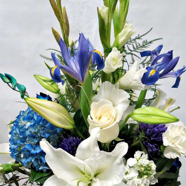 White lilies, blue irises, and a blue hydrangea arrangement in a glass vase