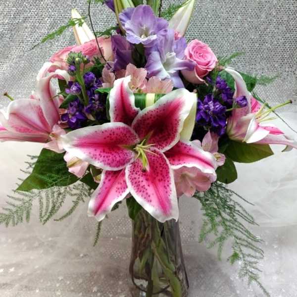 Pink lilies and purple flowers in a tall glass vase