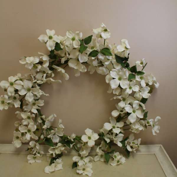 White floral wreath with green leaves on a neutral wall