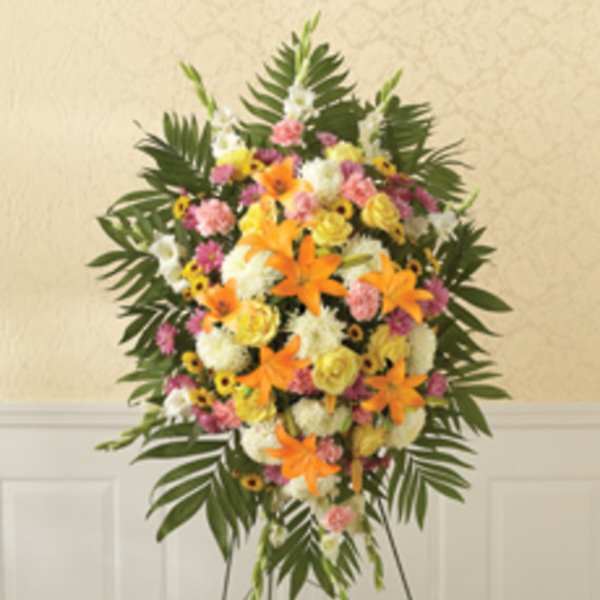 Standing floral spray with orange lilies, pink and white flowers, and palm leaves
