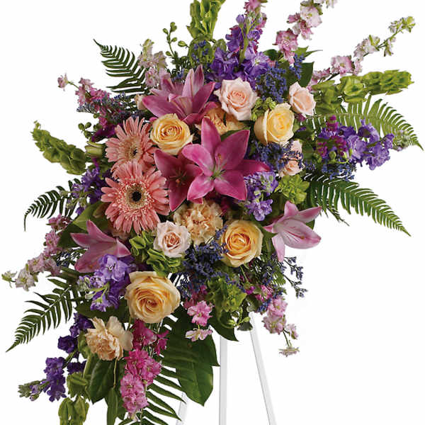 Standing floral spray with pink lilies, roses, and purple blooms on an easel