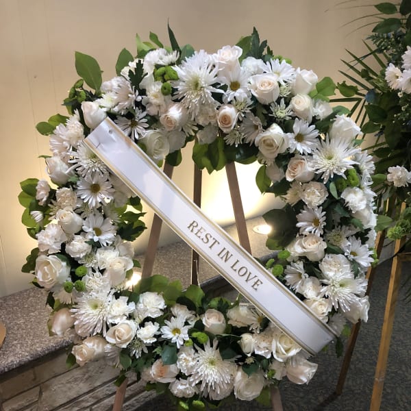 White floral funeral wreath with a "Rest in Love" ribbon
