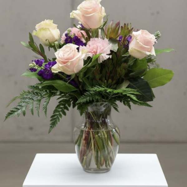 Pink roses and purple flowers arranged in a clear glass vase
