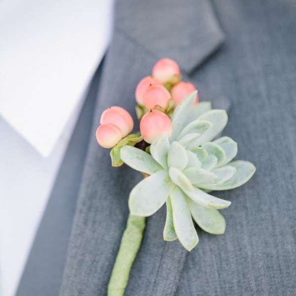Succulent boutonniere with pink berries pinned to a gray suit lapel