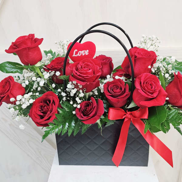 Red roses in a black gift bag with a red heart pick