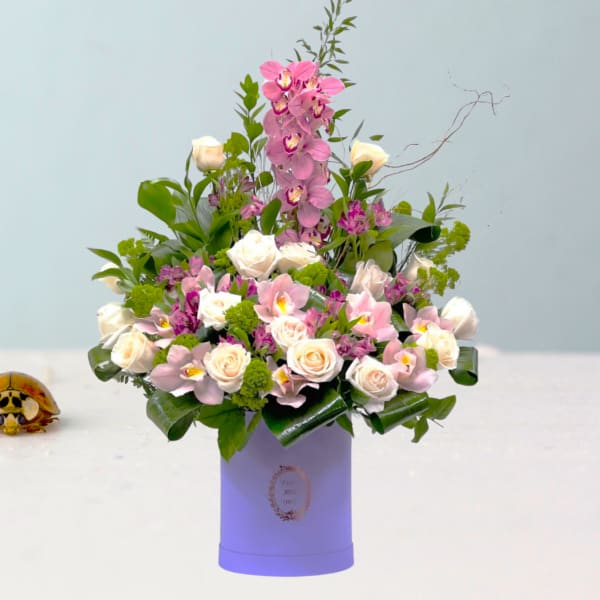 Pink orchids and white roses arranged in a lavender box