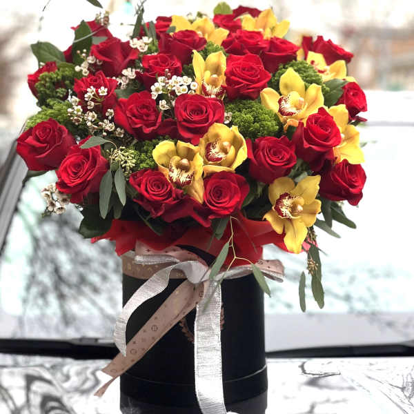 Bouquet of red roses and yellow orchids in a black box with ribbon