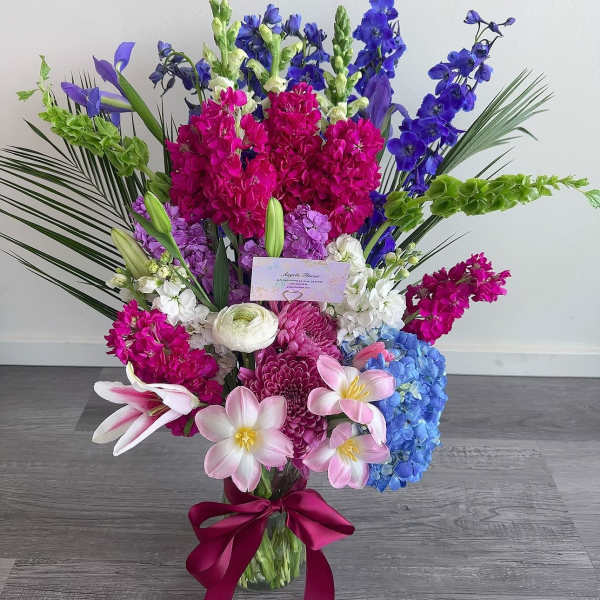 Tall bouquet of pink, blue, purple, and white flowers in a glass vase