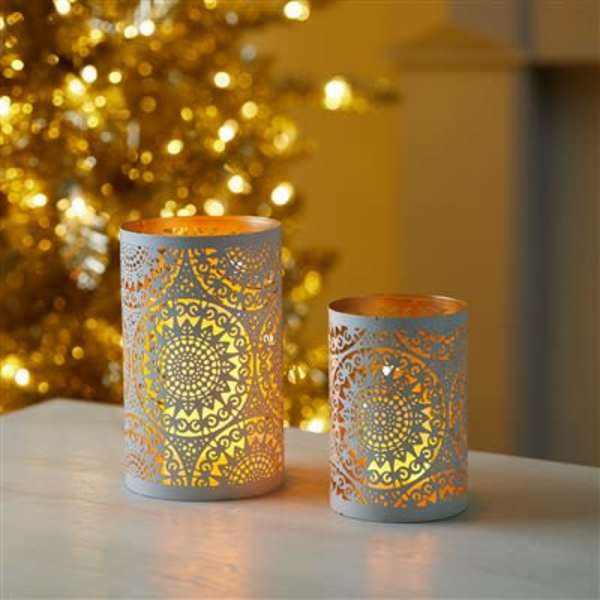 Two decorative candle holders with glowing cutout patterns on a table