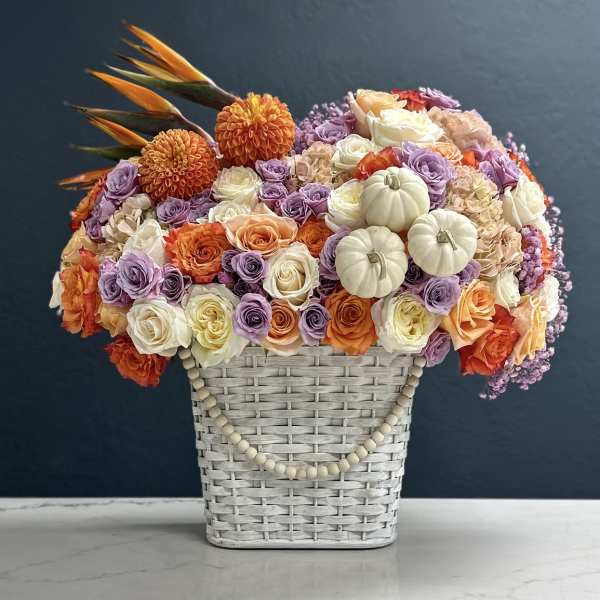 Basket arrangement of roses, dahlias, and small pumpkins