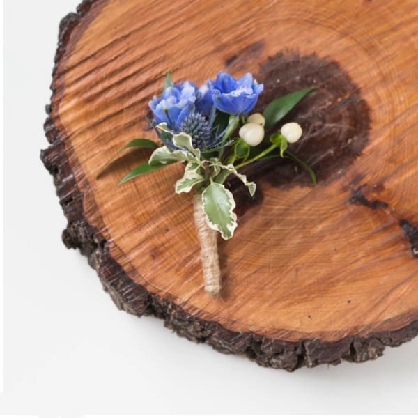 Blue boutonniere with white berries on a wood slice