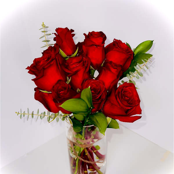 Red roses arranged in a clear glass vase with small greenery accents