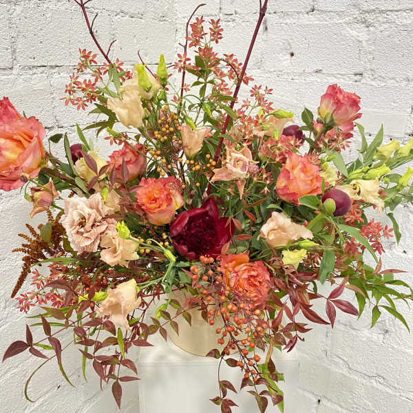 Large mixed floral arrangement in a cream vase with coral and peach blooms