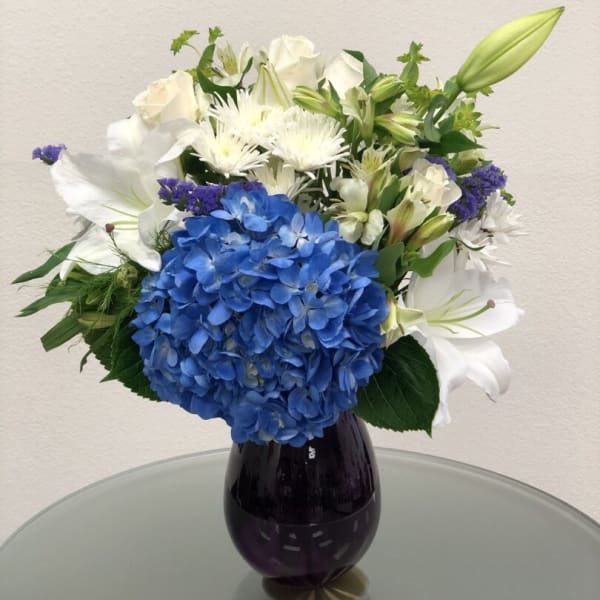 Blue hydrangea bouquet with white lilies and roses in a dark vase