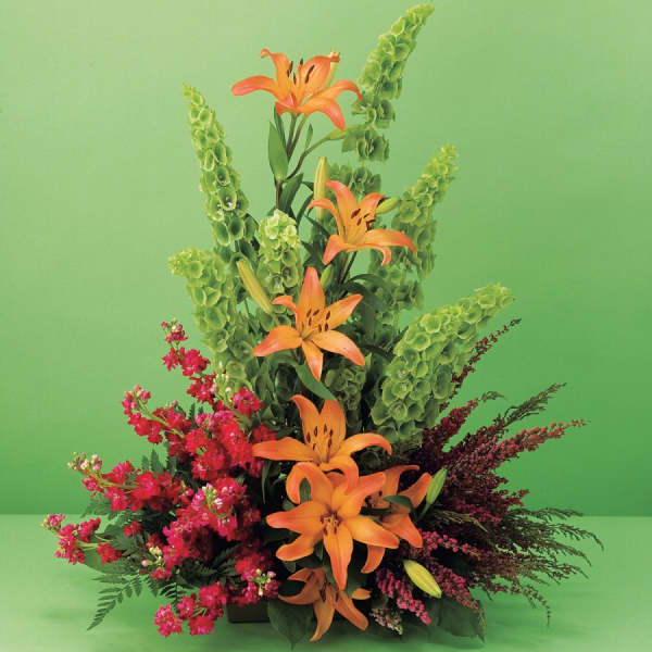 Orange lilies with pink and green floral spikes in a low arrangement