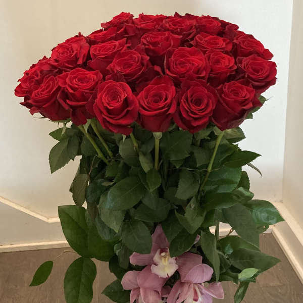Tall bouquet of red roses with pink orchids in a glass vase