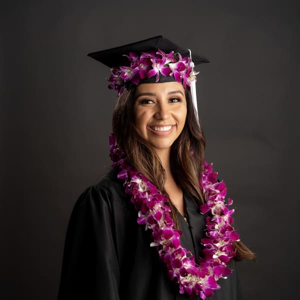 Graduate in a cap and gown wearing a purple orchid lei and matching cap flowers