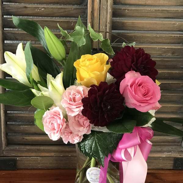 Bouquet of pink and yellow roses with white lilies in a glass vase