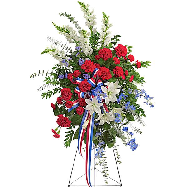 Standing floral spray with red carnations, white lilies, and blue accents on an easel