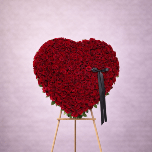 Heart-shaped standing arrangement of red roses on a wooden easel with a black ribbon bow.