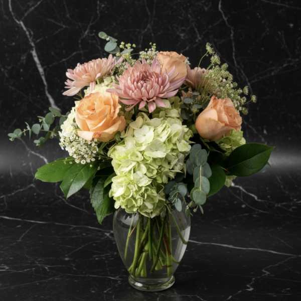 Peach roses and pink blooms in a clear glass vase
