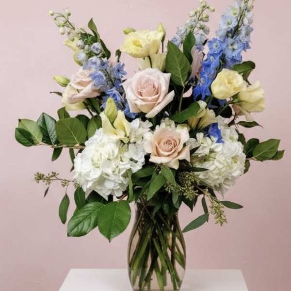Mixed bouquet of pastel roses, hydrangeas, and blue delphinium in a glass vase