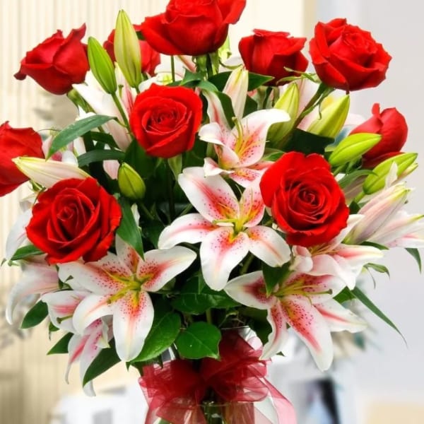 Red roses and white lilies in a clear glass vase with a red ribbon