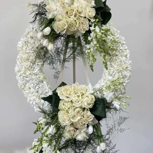 White floral standing wreath on an easel with roses and orchids