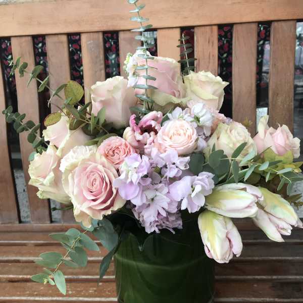Pink and cream roses with pale purple flowers in a green vase