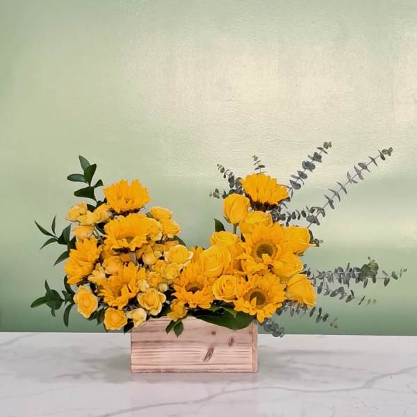Yellow flowers arranged in a wooden box with eucalyptus accents