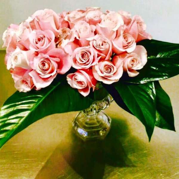 Pink rose bouquet in a clear glass vase with large green leaves
