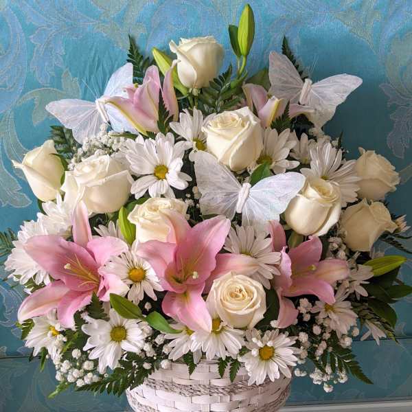 Basket arrangement of white roses, pink lilies, and daisies with butterfly accents