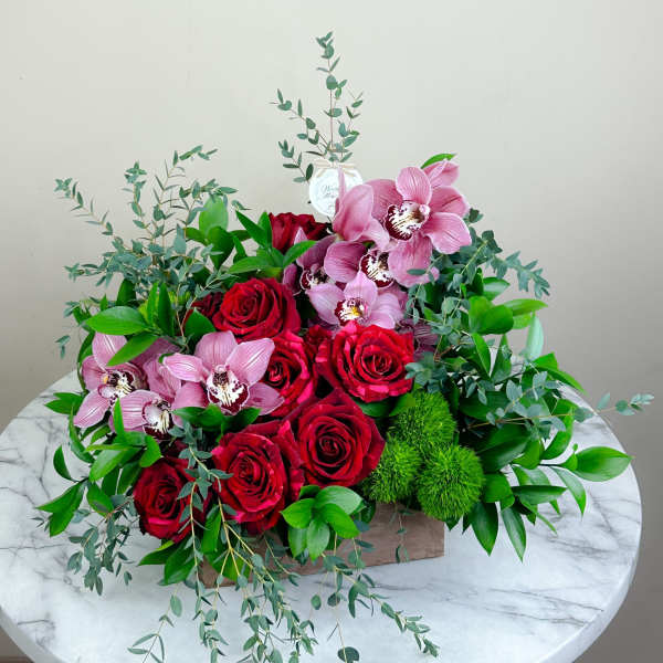 Red roses and pink orchids in a low rectangular arrangement with greenery