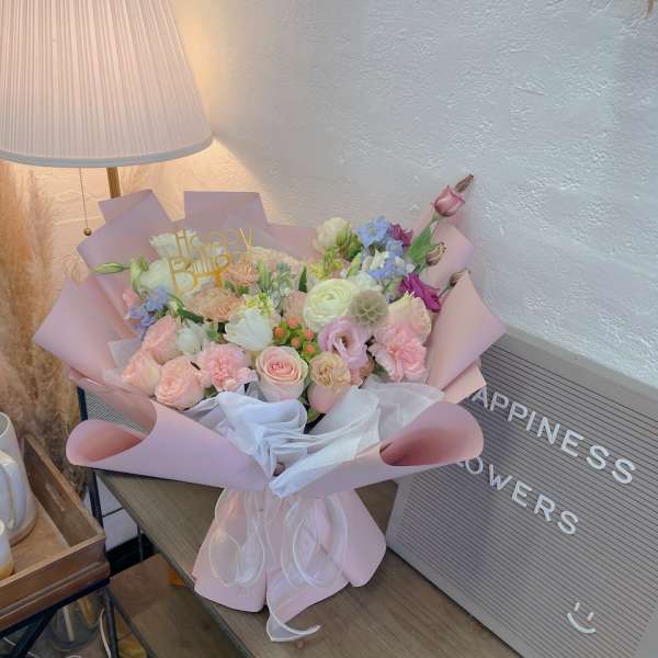 Pastel bouquet of mixed flowers wrapped in pink paper with a birthday topper