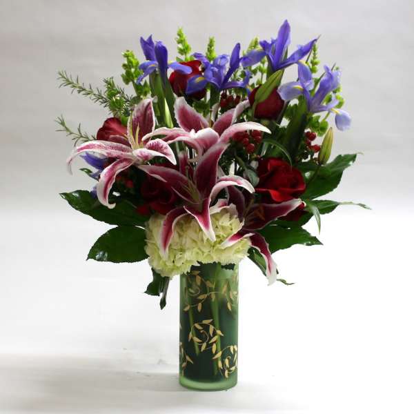 Bouquet of lilies, roses, and irises in a green glass vase