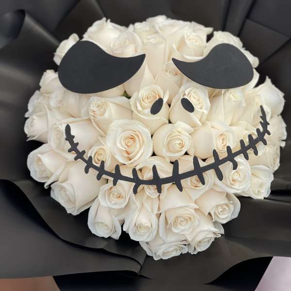 White rose bouquet wrapped in black paper with a skull face design