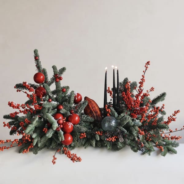 Low holiday centerpiece with evergreen branches, red berries, and black candles