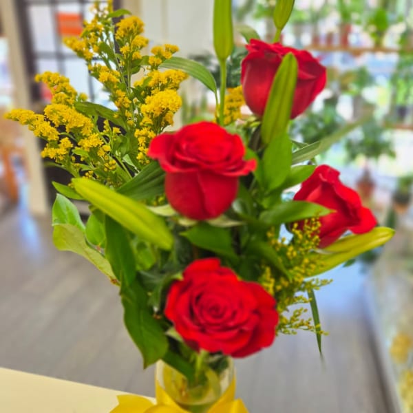 Red roses and yellow filler flowers in a clear glass vase