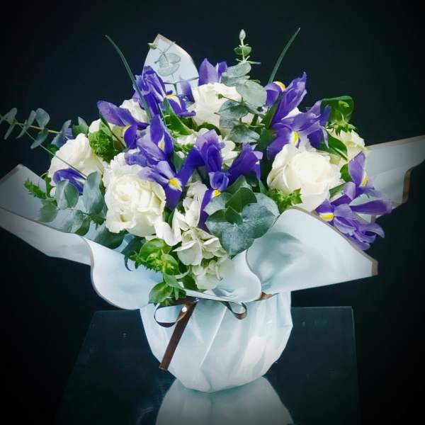 Compact bouquet of purple irises and white roses in light blue wrap with ribbon