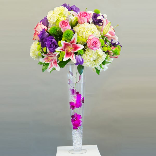 Tall bouquet of pink roses, lilies, and purple flowers in a clear vase