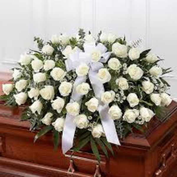 White rose casket spray with ribbon on a wooden casket