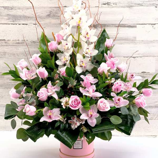 Pink roses and white orchids in a pink hatbox arrangement
