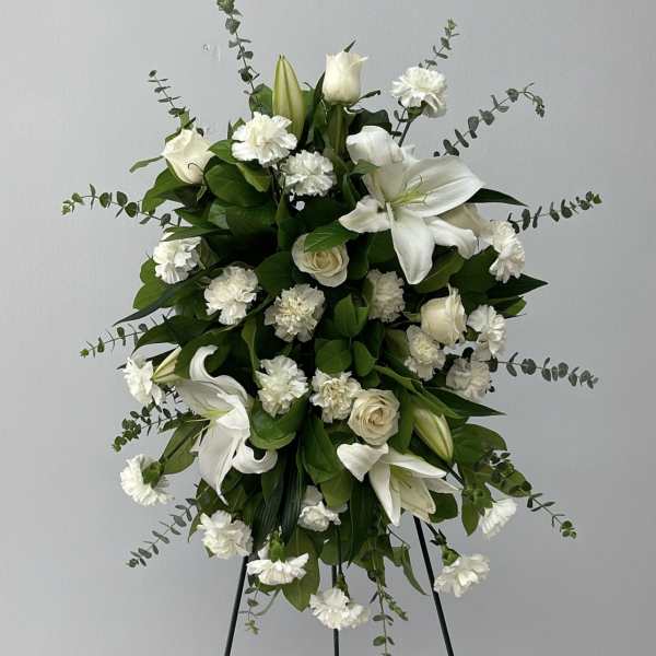 White floral standing spray with lilies, roses, and carnations on a black easel