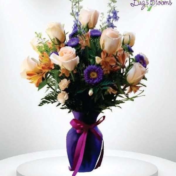 Bouquet of pale roses and purple flowers in a purple vase with ribbon