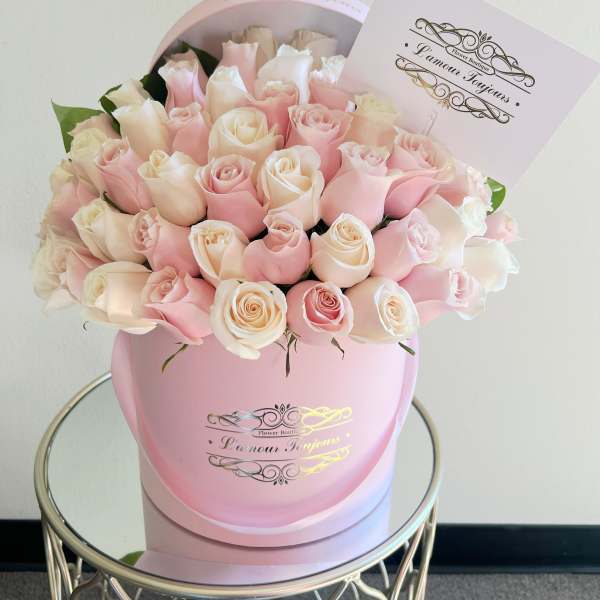 Pink and white roses arranged in a round pink box with a card.