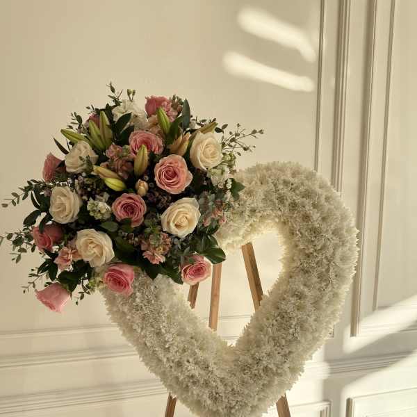 Heart-shaped white floral wreath with pink roses on a wooden easel